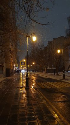 an empty city street at night with snow falling on the ground and people walking down the sidewalk