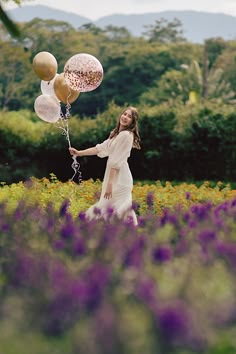 a woman in a field holding onto some balloons