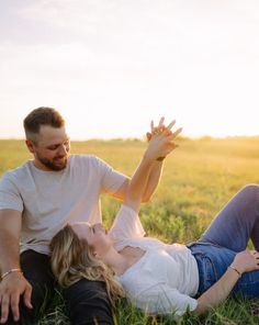 a man and woman laying on the ground in a field with their arms around each other