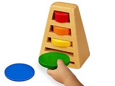 a child's hand is playing with a wooden toy stacking tower and matching discs