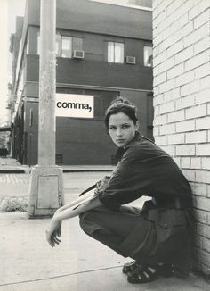 black and white photograph of a young man leaning against a brick wall on the sidewalk