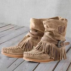 a pair of brown boots with fringes and buckles sitting on top of a wooden floor