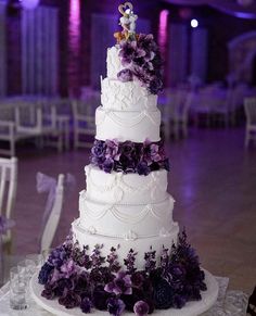 a white wedding cake with purple flowers on the top and bottom tier is sitting on a table