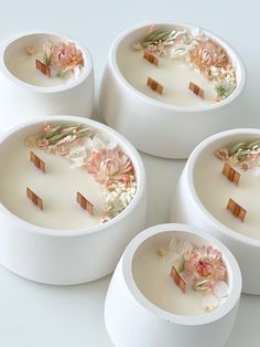 four white bowls with flowers and sticks in them