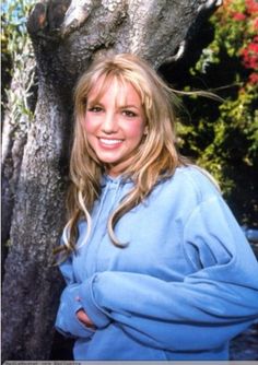 a woman standing in front of a tree with her arms crossed and looking at the camera