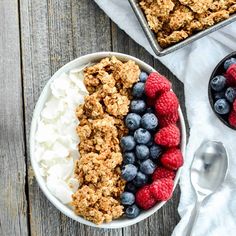 a bowl filled with granola, blueberries and raspberries next to a spoon