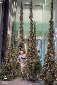 a man standing in front of christmas trees with lights on them and garlands hanging from the ceiling