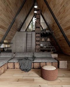 a loft with wooden walls and flooring has a large couch in the middle, surrounded by wood planks