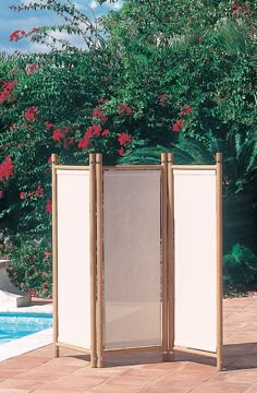 an outdoor room divider in front of a swimming pool with trees and bushes behind it