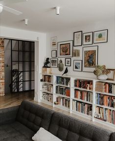 a living room filled with lots of books and pictures on the wall next to a couch