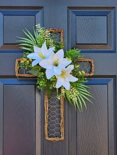 a cross decorated with flowers and greenery hangs on the front door of a house