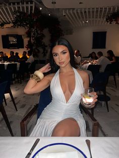 a woman in a white dress sitting at a table with food and drinks on it