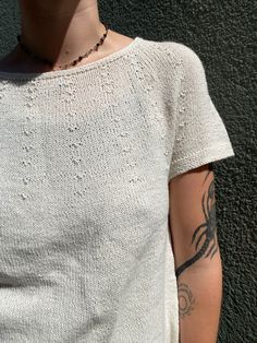 a woman with tattoos on her arm standing in front of a wall wearing a white shirt