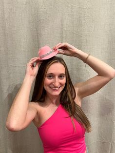 a woman in a pink tank top is smiling and holding her hat over her head