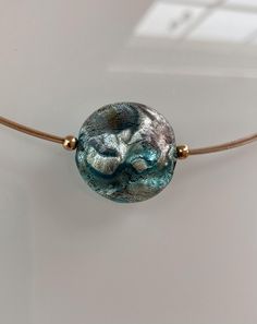 This contemporary necklace features an amazing Murano glass bead.  The lentil shape bead is puffy in the middle and thinner on the sides.  It has a diameter of 20mm (25/32in). Shades of aqua, silver and green are combined with white gold foil creating a rich texture in a unique abstract pattern. The result is so gorgeous that it was hard to stop taking pictures =) it is elegantly enhanced by three strands of wire.   The high quality wire is strong and flexible. It is made of stainless steel plated with gold and covered with nylon to prevent tarnish. All metal components are made of 14kt gold filled*, including the 5cm (2in) extender chain. Measurement Conversion Table: 16 in = 43 cm 18 in = 46 cm 20 in = 51 cm * GOLD FILLED is to be distinguished from gold plated which has a very thin laye Adjustable Glass Pendant Beaded Necklaces, Adjustable Glass Beaded Pendant Necklaces, Elegant Iridescent Glass Necklaces, Adjustable Murano Glass Necklace, Adjustable Round Murano Glass Necklace, Adjustable Glass Round Pendant Necklace, Iridescent Round Glass Bead Jewelry, Iridescent Round Glass Beads Jewelry, Iridescent Glass Jewelry With Round Beads