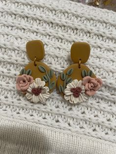 a pair of earrings with flowers on them sitting on top of a white knit surface