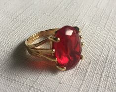 Elegant solitaire red ring set in a gold setting. The gemstone measures .75" by .5"  and it's set in a 18 Kt Electroplated Gold setting. (It says 18 Kt GE inside.) Size 5.75 or maybe 6. Please know that if you don't like the way the ring fits, you can return it; you pay for the shipping, but there's no restocking fee or questions asked, I just refund the ring's cost to you. Please take a look at my storefront at: https://www.etsy.com/shop/FabFinds42?ref=seller-platform-mcnav I have a wide select Red Gem Ring, Gold Ring Big, Red Ring, Red Rings, Red Jewel, Costume Rings, Chunky Ring, Jewels Rings, Chunky Jewelry