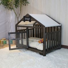 a small wooden dollhouse bed with a white sheet on the floor next to a potted plant