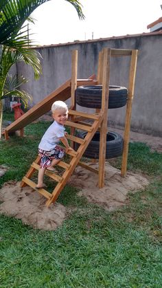 a little boy climbing up a wooden ladder in the grass next to a tire track