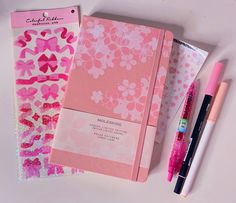 pink notebooks and pens on a white surface next to each other, with the cover covered in flowers