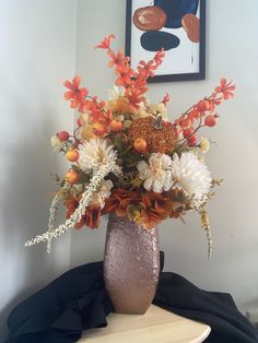 a vase filled with lots of flowers sitting on top of a table next to a painting