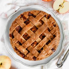 an apple pie with latticed crust on a white plate next to sliced apples and utensils