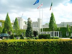 a large white building with flags flying in the wind next to a lush green hedge