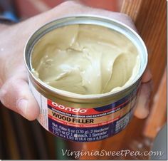 a person holding a can of wood filler in their hand with the lid open