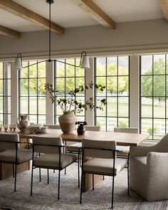 a dining room table with chairs and vases on top of it in front of large windows