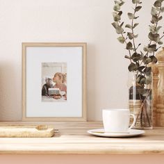 a coffee cup sitting on top of a wooden table next to a vase with flowers