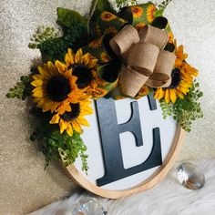 sunflowers and greenery are arranged around the letter e on a wooden plaque