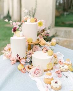 three white cakes sitting on top of a table covered in flowers and doughnuts