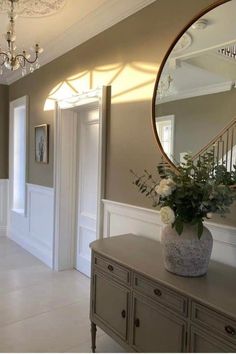 a vase with flowers sitting on top of a dresser next to a mirror and chandelier