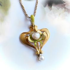 "Found is this beautiful gold and pearl lavalier pendant from the Art Nouveau (ca 1910) era. This delicate piece is made of vibrant, brushed 14k yellow gold and has a flowing stylized heart shape approx. 32 mm long x 21 mm wide x ⅛\" thick. The pendant has a leaf motif with delicate, leaf-like swirls adorned with soft enameling in hues of green and yellow. In the center of the pendant is a single freshwater pearl.  Dangling freely from the base of the pendant is another l4.2 mm x 5mm  pearl. The Gold Art Deco Necklace With Pearl Pendant, Yellow Gold Art Nouveau Jewelry For Anniversary, Art Nouveau Yellow Gold Jewelry For Anniversary, Victorian Yellow Gold Heart Pendant Necklace, Collectible Art Nouveau Yellow Gold Jewelry, Vintage Heart Pendant Jewelry With Pearl, Art Nouveau Yellow Gold Pendant Jewelry, Art Nouveau Yellow Gold Necklace For Formal Occasions, Elegant Flower Pendant Jewelry Collectible