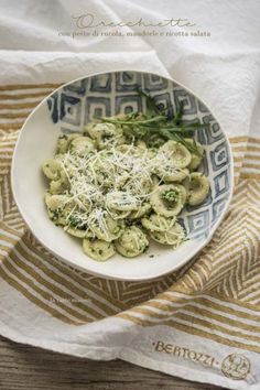 pasta with pesto and parmesan cheese in a white bowl on a striped towel