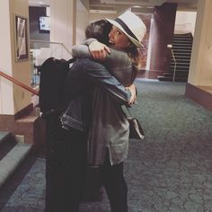 two people hugging each other in an airport lobby with stairs leading up to the second floor