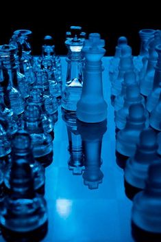 a large group of glass chess pieces sitting on top of a white table with blue lighting