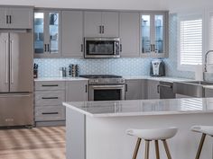 a modern kitchen with stainless steel appliances and white counter tops, along with stools