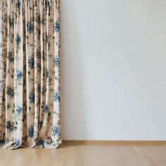 an empty room with a curtain and wooden floor in front of the white wall that has blue flowers on it