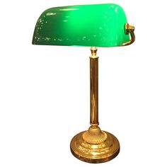 a green glass lamp sitting on top of a metal stand with a gold plated base