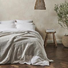 a bed with white linens and pillows in a bedroom next to a potted plant