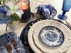 a blue and white table setting with plates, silverware, candlesticks and flowers