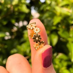 a woman's finger with a ring made out of flowers on it and gold leaves