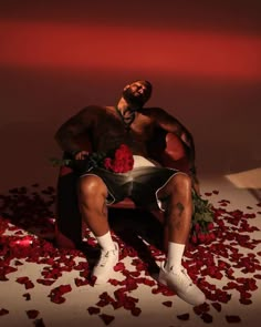 a man sitting on top of a chair surrounded by rose petals with his hands in his pockets