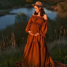 a pregnant woman in an orange dress and hat poses for the camera while wearing a brown hat