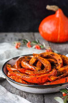 a bowl filled with cooked carrots on top of a table next to a pumpkin