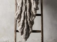 a large pile of fur hanging from a ladder next to a white wall and wooden chair