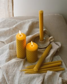 three yellow candles sitting on top of a bed next to two forks and spoons