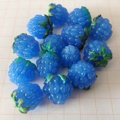 some blue raspberries are sitting on a white table top and there is no image here to provide a caption for