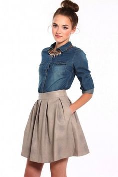 a woman in a skirt and denim shirt posing for the camera with her hands on her hips